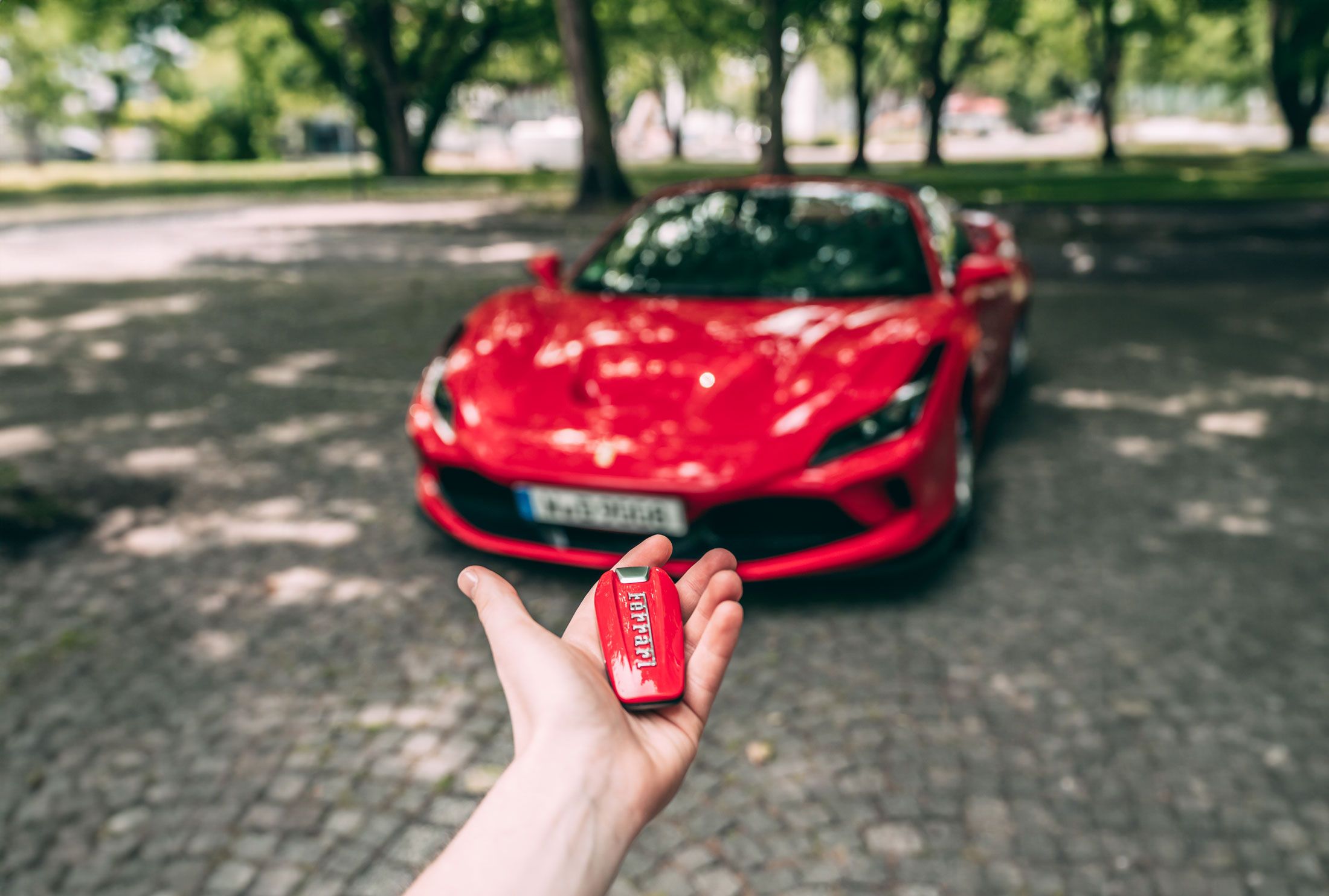 Mann präsentiert Schlüssel seines Ferraris mit dem Auto im Hintergrund